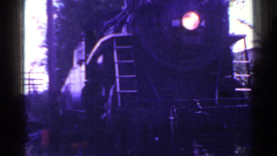 A close 1953 Connecticut view shows the steam locomotive front and headlight passing near the camera, with vegetation and smoke around the track.