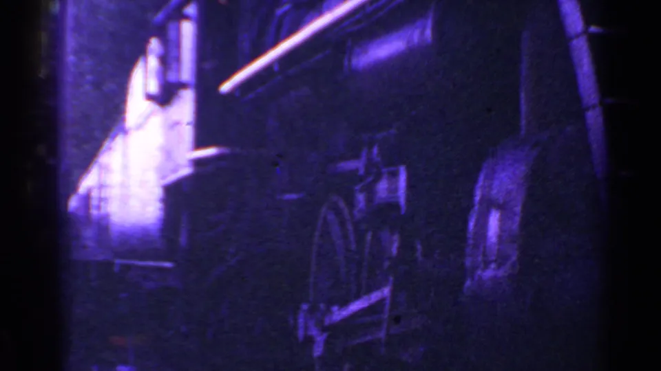 The train passes beside the camera in the 1953 Connecticut footage, revealing the locomotive side, large wheel area, piping, smoke, and blue-purple film cast.