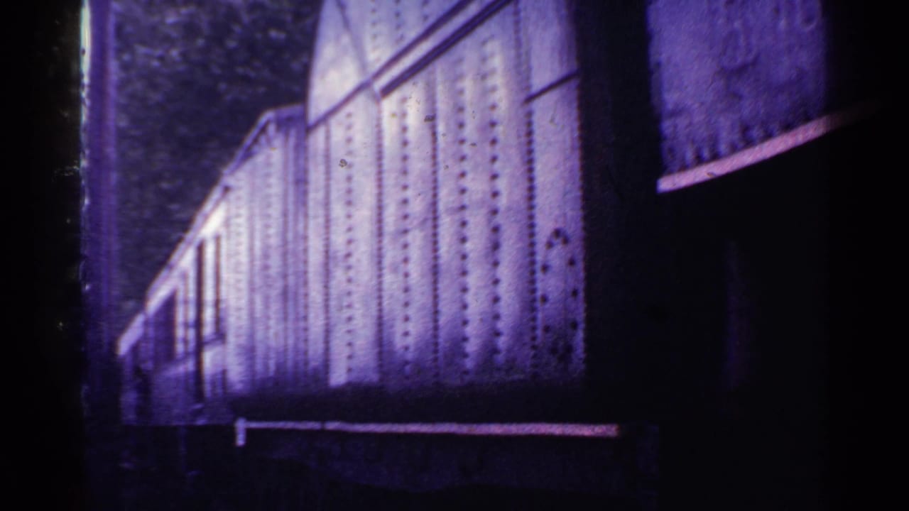 1953 Connecticut 8mm frame showing the side of a riveted train car moving past in a purple-tinted, soft-focus trackside view.