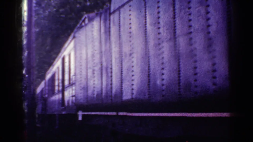 1953 Connecticut 8mm frame of a passing riveted railcar, heavily tinted purple with visible film borders and soft archival grain.