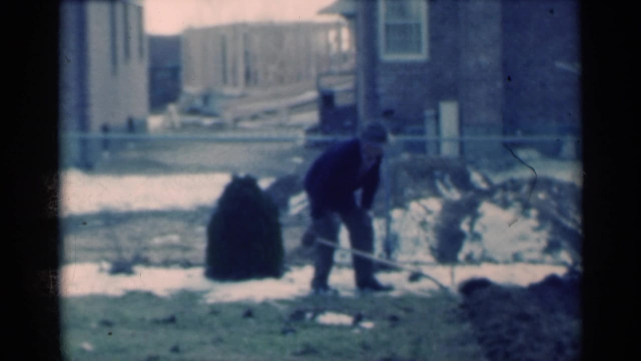 Man bends forward with a shovel beside snow and exposed soil.