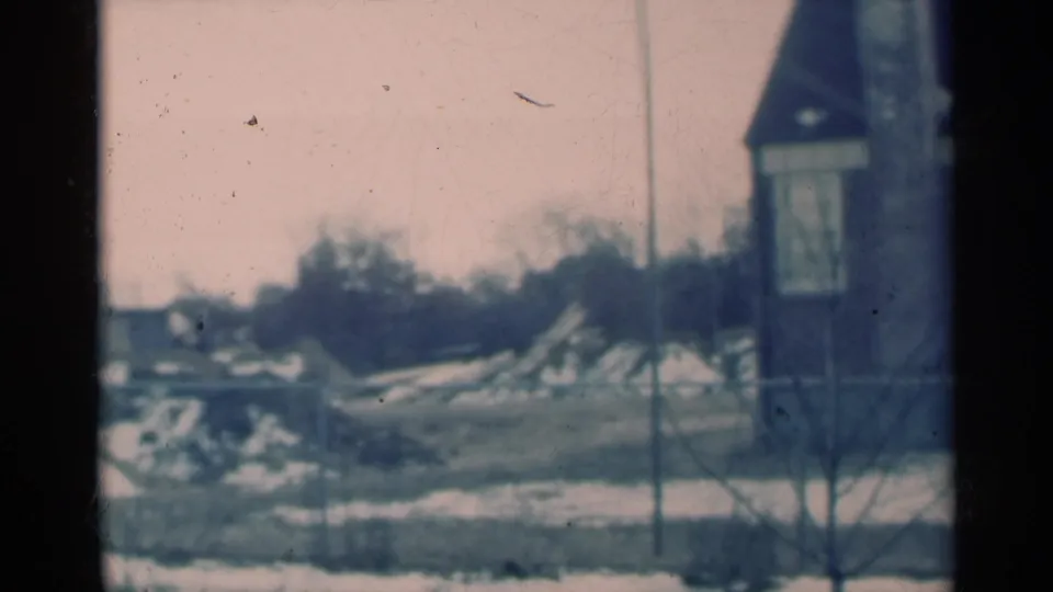 1939 Michigan 8mm frame showing a snow-dusted rural landscape through a window, with bare trees and a small tower-like structure.