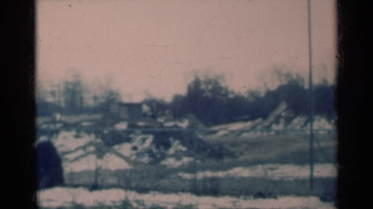 1939 Michigan home-movie frame of a quiet snow-dusted rural or small-town landscape with bare trees and distant structures.