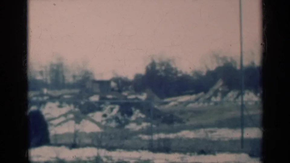 1939 Michigan home-movie frame of a quiet snow-dusted rural or small-town landscape with bare trees and distant structures.