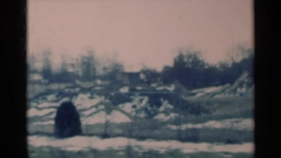 1939 Michigan 8mm view across snow patches and bare trees toward distant buildings, framed by dark vertical window edges.