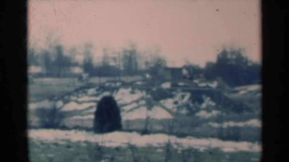 Soft 1939 Michigan home-movie frame of snow patches, bare trees, low fencing, and distant rural structures.