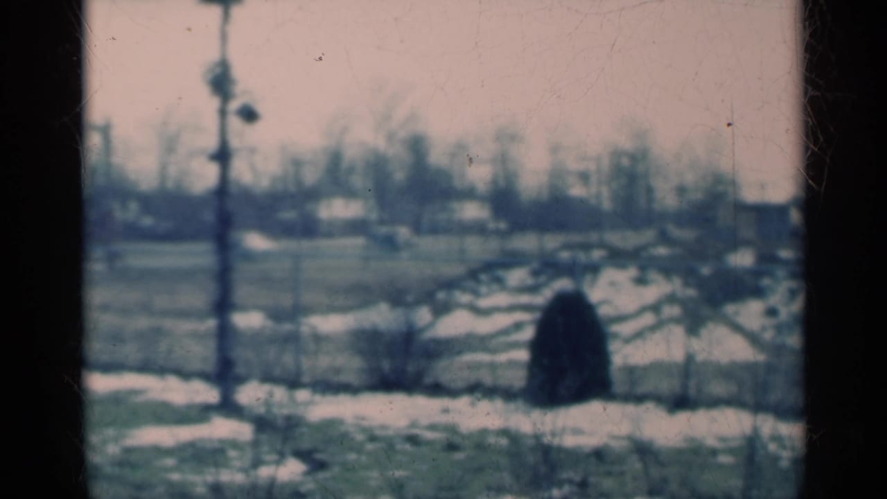 1939 Michigan 8mm frame of a static rural winter landscape with snow patches, distant homes, bare trees, and faded color.
