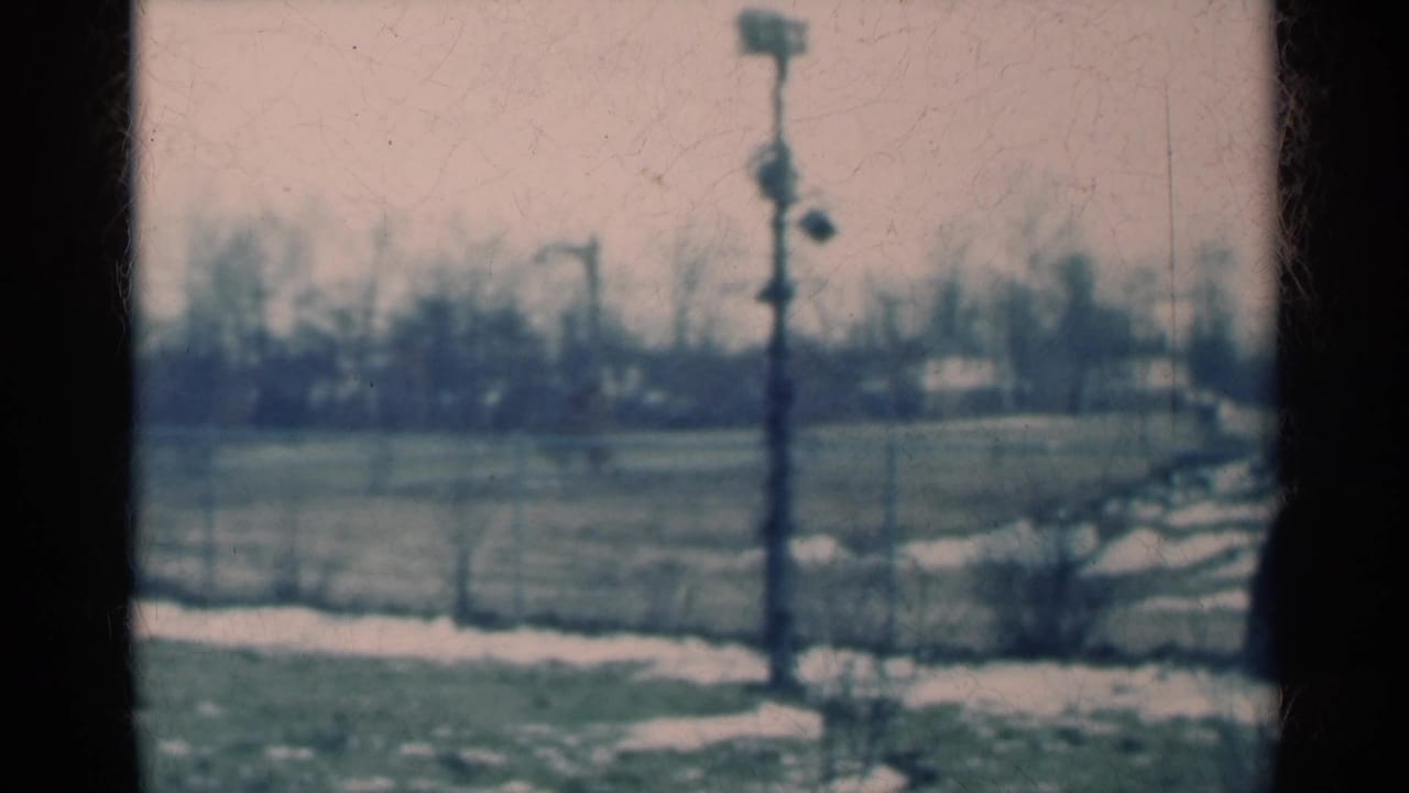 1939 Michigan 8mm still with a central utility pole, patchy snow on grass, a pale path, and soft distant trees.