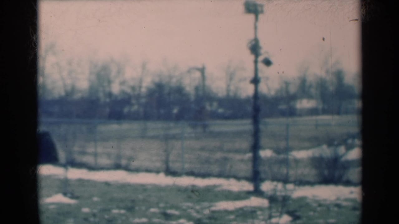 1939 Michigan rural frame showing a snow-patched field, utility pole, bare horizon trees, and a dark rounded form partly cut off at left.