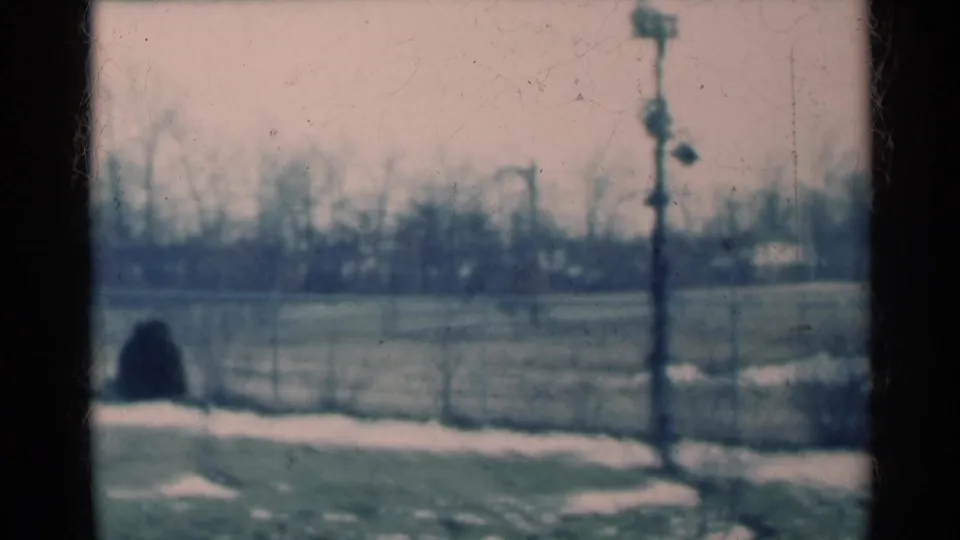 1939 Michigan 8mm frame looking from inside a house toward a snow-dusted yard, chain-link fence, bare trees and a utility pole.