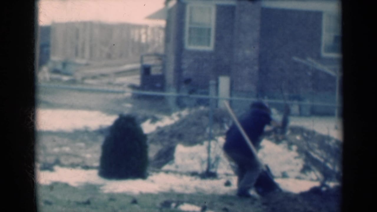 Michigan 1939 frame showing the man bent toward the frozen ground while working near snow and a small evergreen bush.