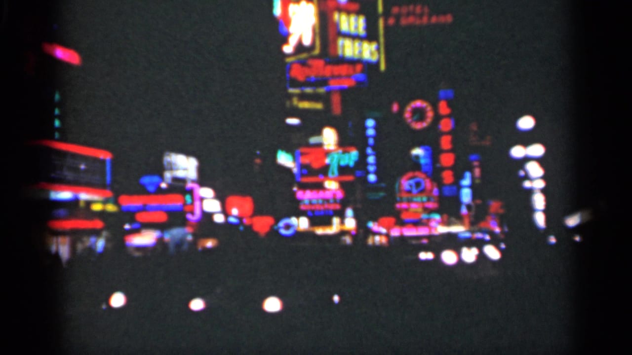 Blurred nighttime street with colorful neon signs and bright car headlights.