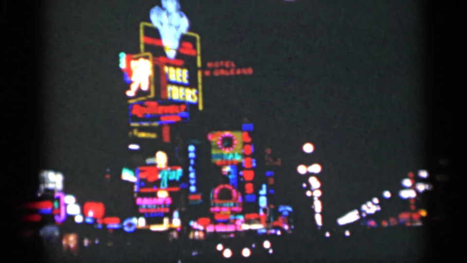 1949 New Orleans street scene with a prominent vertical neon sign, surrounding glowing signs, and headlight trails on 8mm film.
