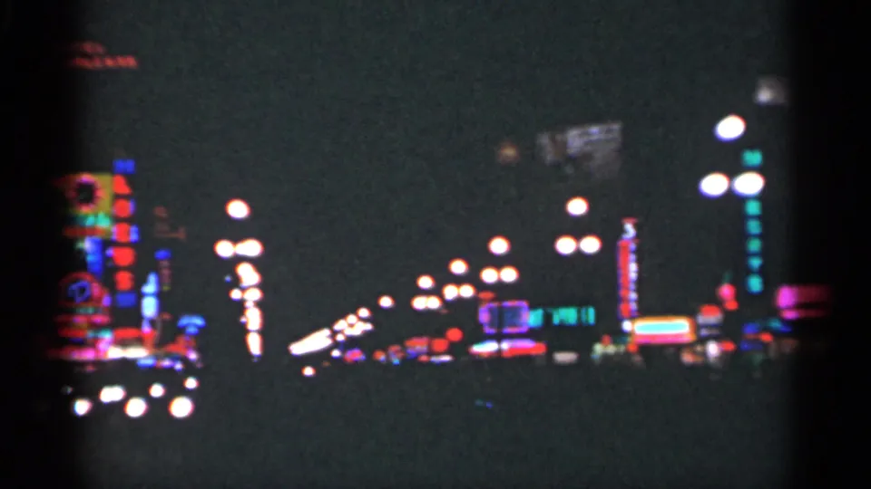 1949 New Orleans nighttime street view with receding streetlights, scattered neon signs, and dark foreground from a home-movie camera.