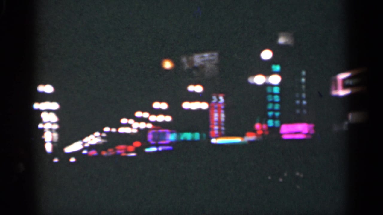 Night street with rows of lights and blurred neon signs along a dark sidewalk.