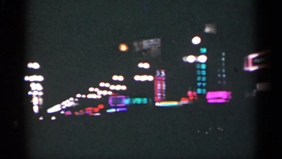1949 New Orleans night street seen on 8mm film, with rows of streetlights, soft neon signs, and dark sidewalk silhouettes.