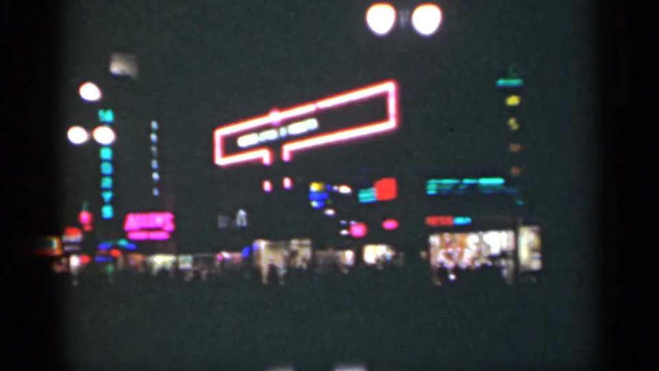 1949 New Orleans street at night, showing a large neon sign, bright storefronts, and indistinct pedestrian silhouettes below.