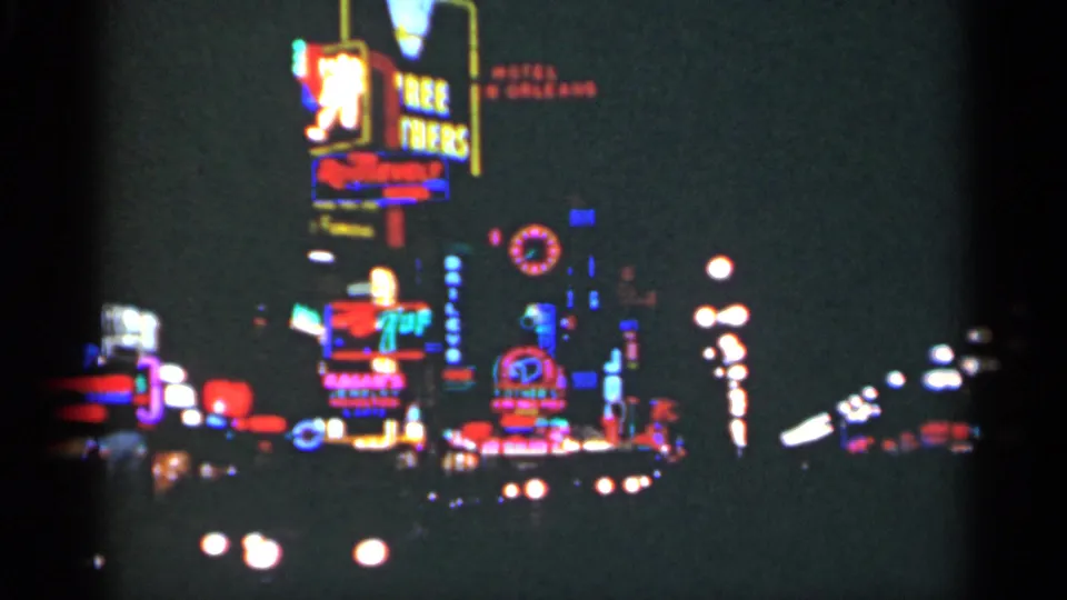1949 New Orleans nighttime 8mm view with colorful neon advertising, distant headlights, and a dark commercial street.
