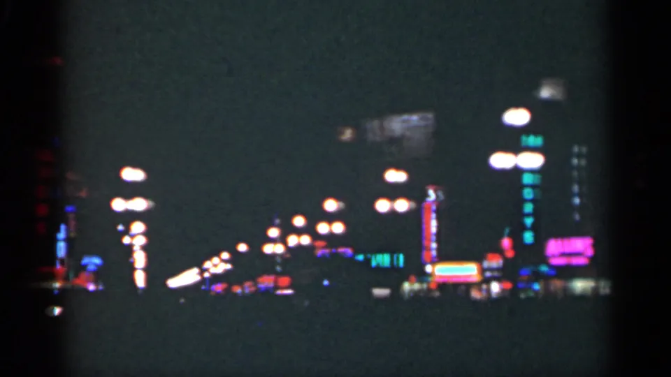 Grainy 8mm view of a New Orleans street lined with neon motel and commercial signs at night.
