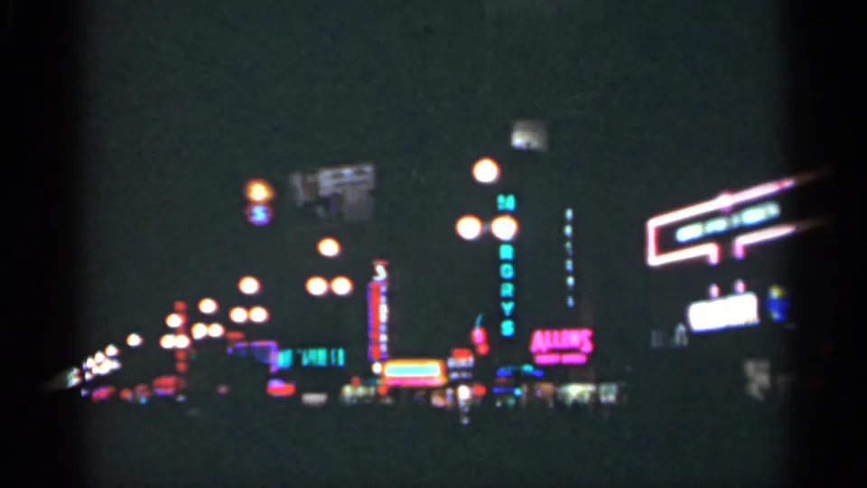1949 New Orleans night footage showing a vertical motel sign, glowing neon storefronts, streetlights, and distant traffic.