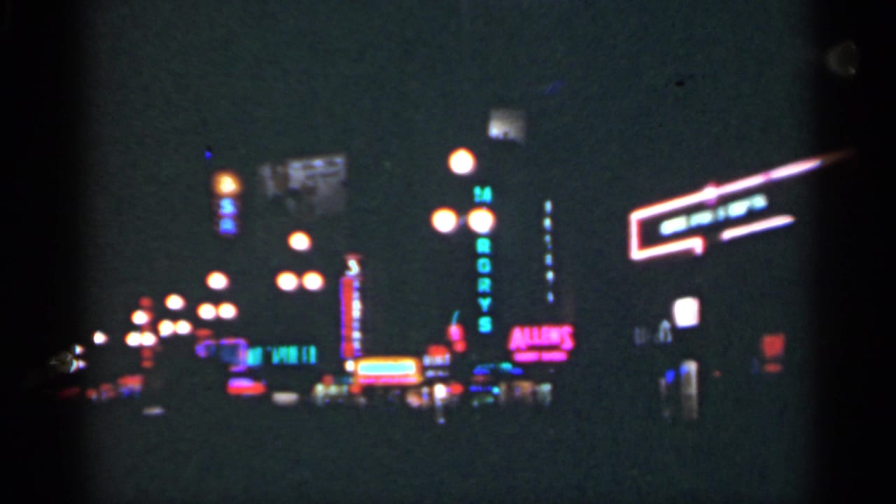 1949 New Orleans night street view with blurred neon signs, glowing streetlamps, and dark building silhouettes on 8mm film.