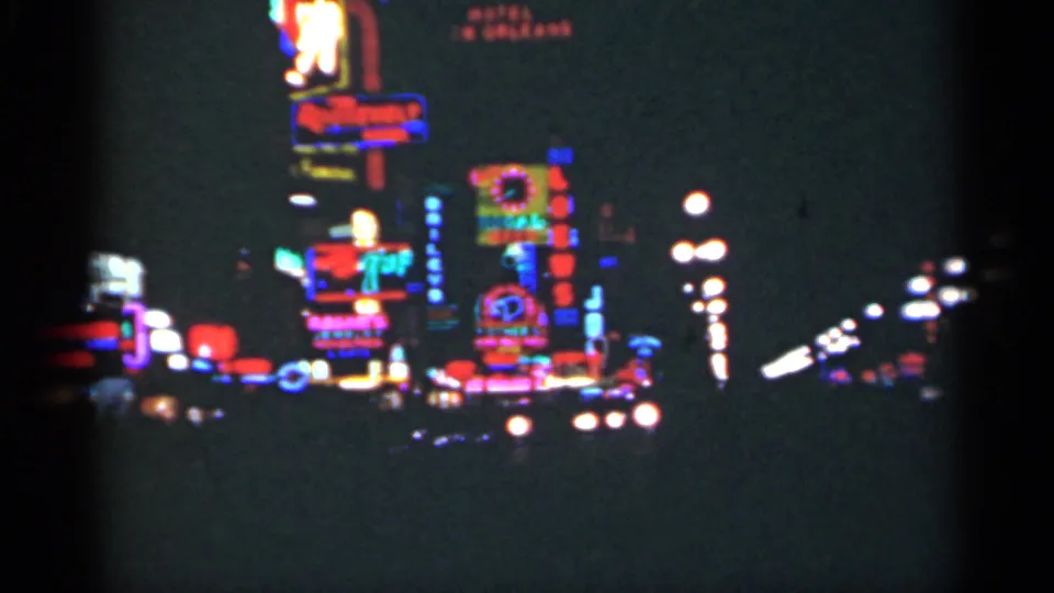 A concentrated group of New Orleans neon signs and streetlights glows against dark building fronts in 1949 8mm footage.