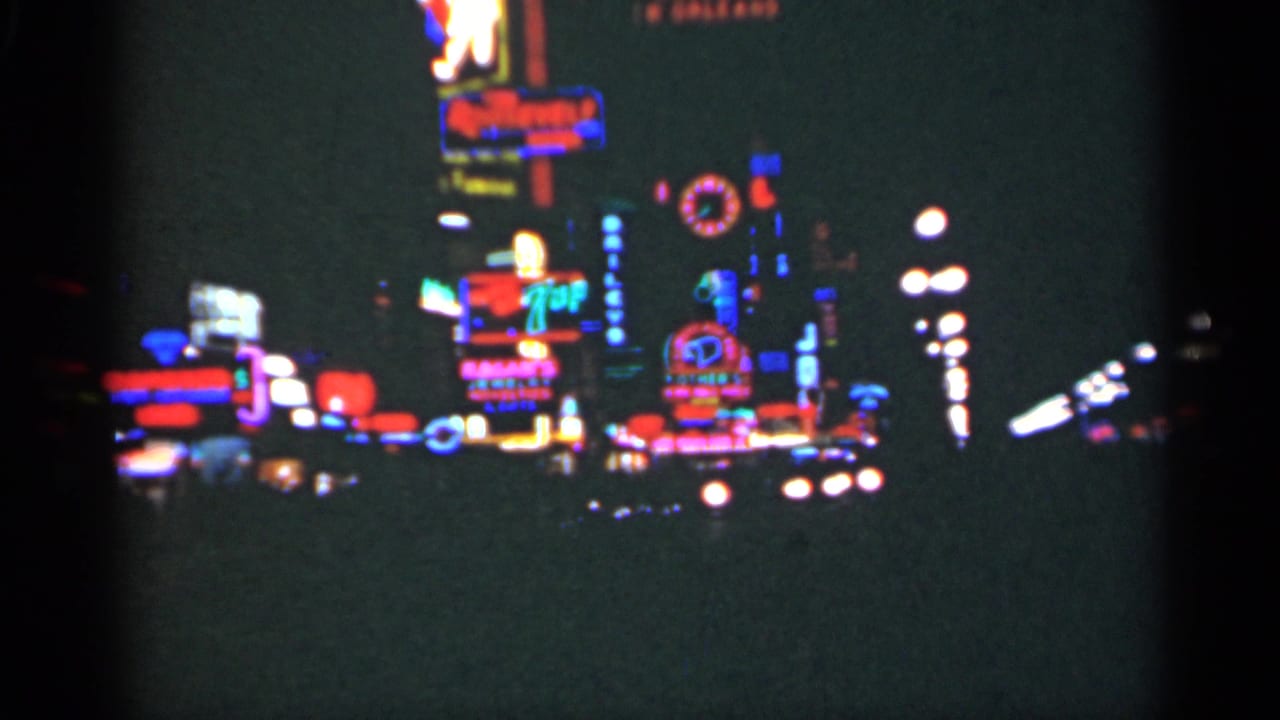 Soft night view of clustered neon signs and streetlights along a dark city street.