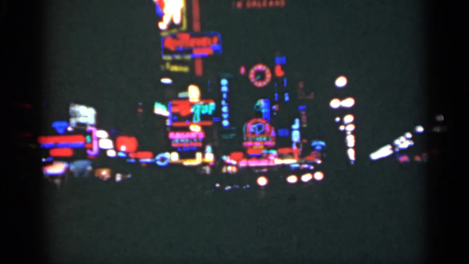 1949 New Orleans home-movie frame showing blurred neon signs, streetlights, and dark roadway silhouettes at night.