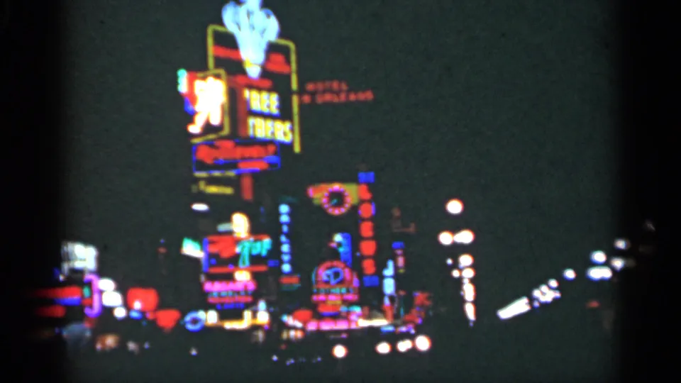 1949 New Orleans frame with tall stacked neon signage, streetlamps, and soft traffic lights in 8mm color.