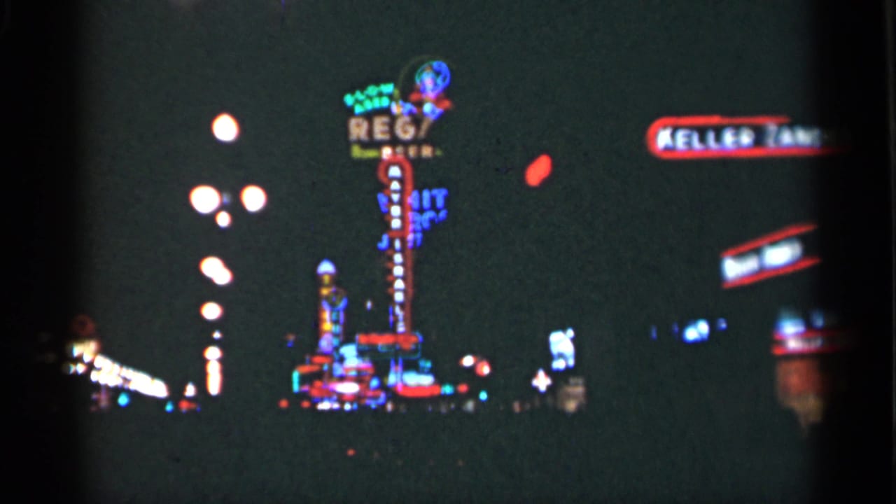 1949 New Orleans home-movie frame with bright neon signs, globe streetlights, and a dark commercial street seen from a moving viewpoint.