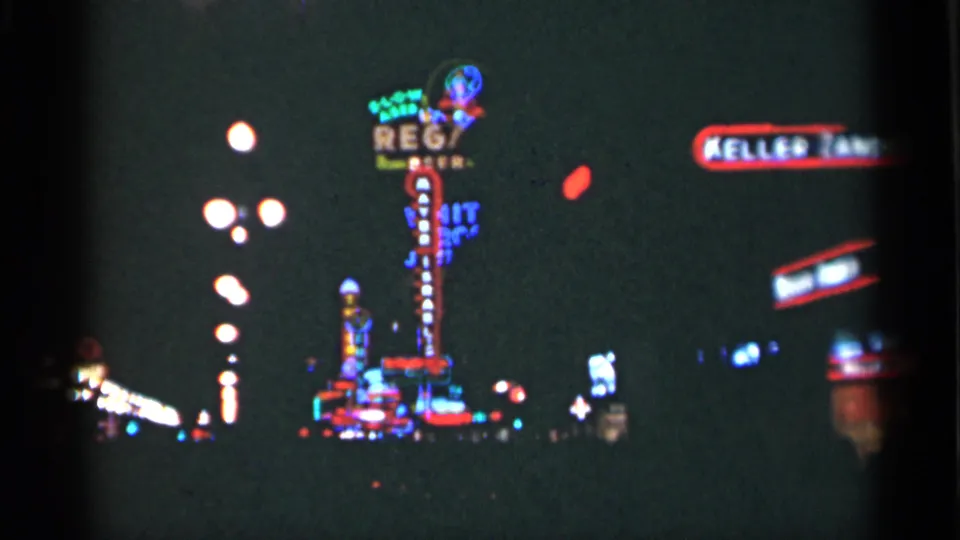 1949 New Orleans home-movie frame with bright neon signs, globe streetlights, and a dark commercial street seen from a moving viewpoint.