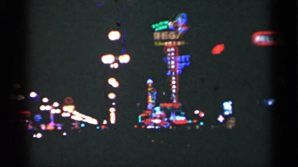 1949 New Orleans nighttime frame showing tall neon signage, repeated streetlamps, and blurred lights from a moving home-movie camera.