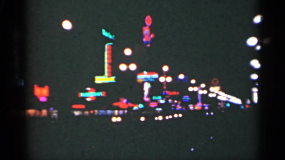 1949 New Orleans home-movie frame showing neon signage and rows of bright streetlights in a nighttime commercial area.
