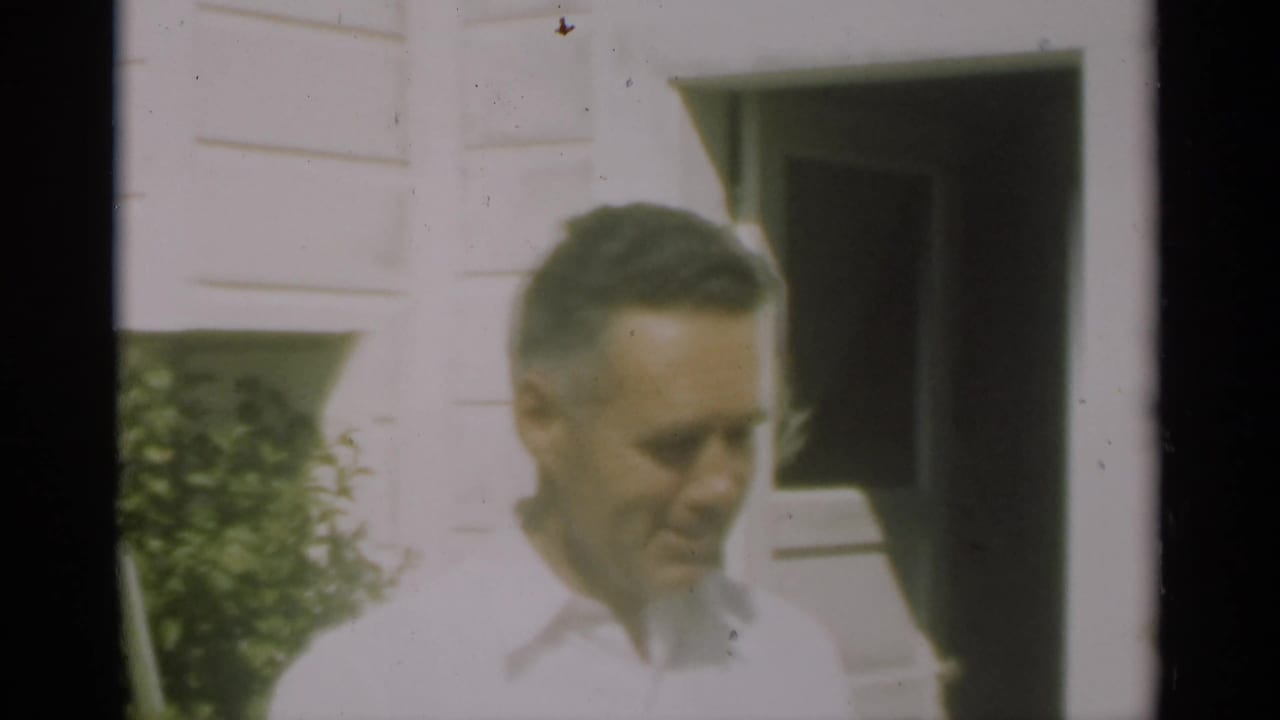 Man in a light shirt smiling near an exterior doorway.