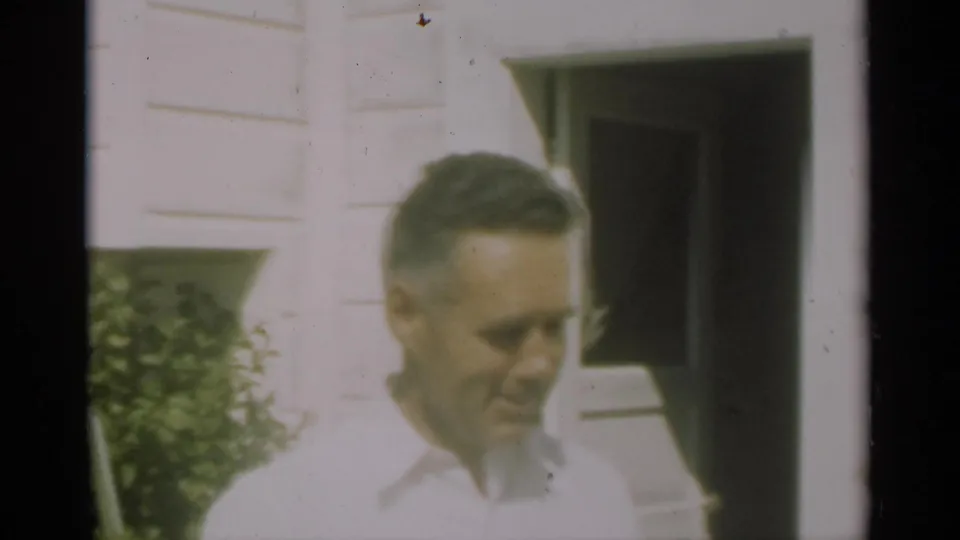 In 1949 New Orleans home-movie footage, a man in a light shirt smiles near a white clapboard wall and dark doorway.
