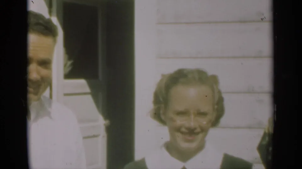 A man and a woman with glasses appear outside a white clapboard house in the 1949 New Orleans home-movie clip.