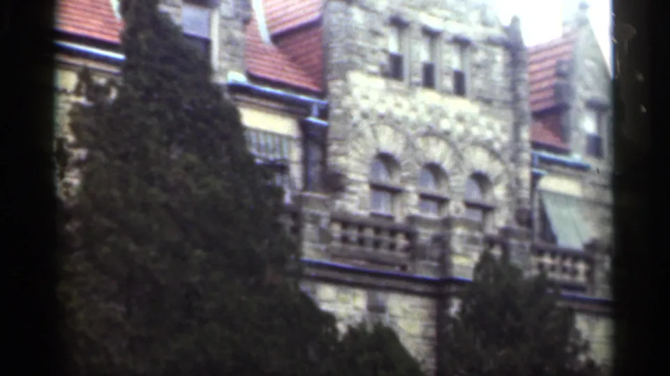 1949 New Orleans frame showing red tile roof sections, stone gables, arched windows, awnings, and foreground evergreens.