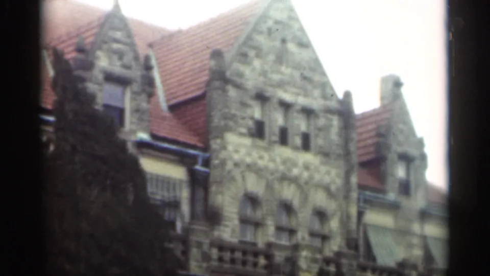 1949 New Orleans home-movie frame of a gabled stone building with red tile roof, arched facade, awnings, and trees.
