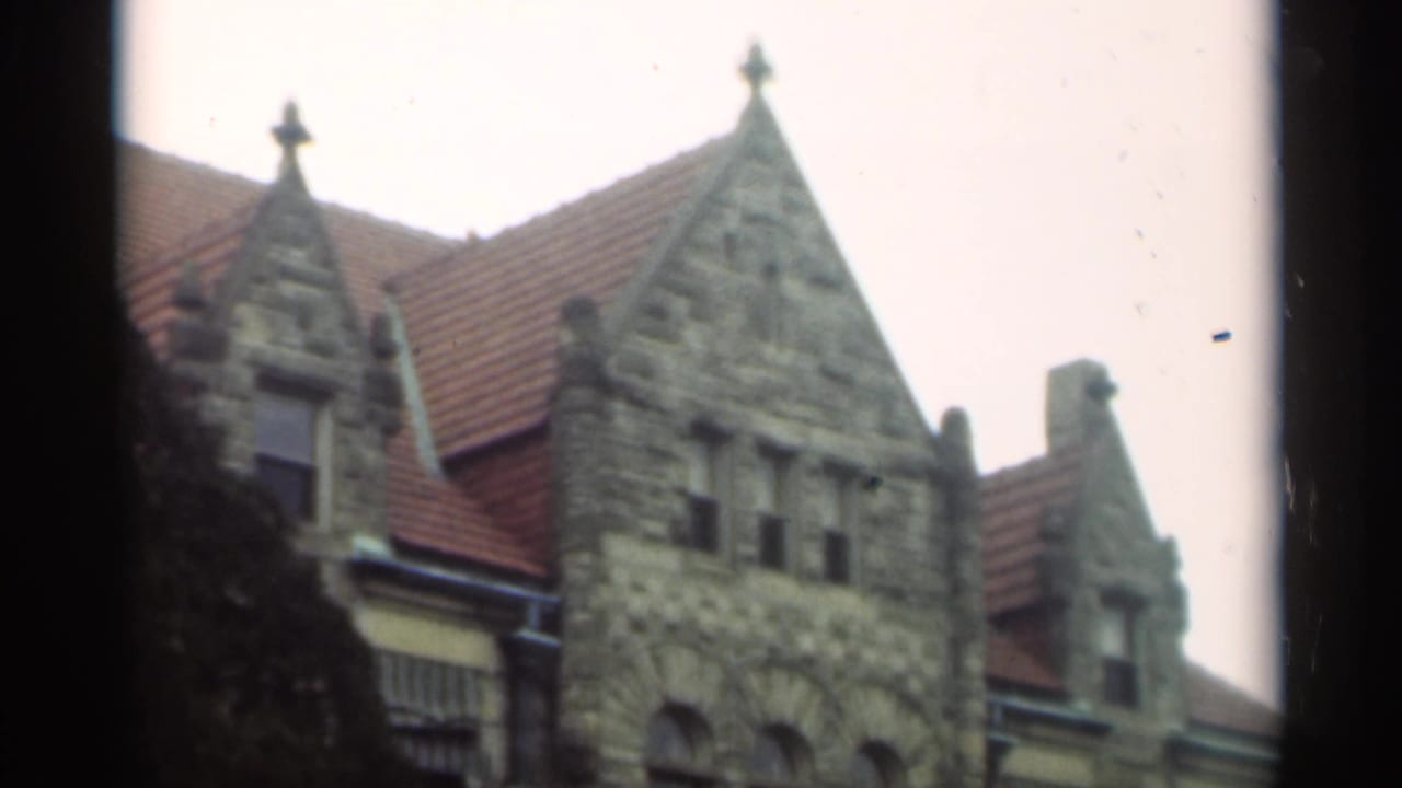 Stone gabled building with red tile roof and dark tree branches at the left edge.