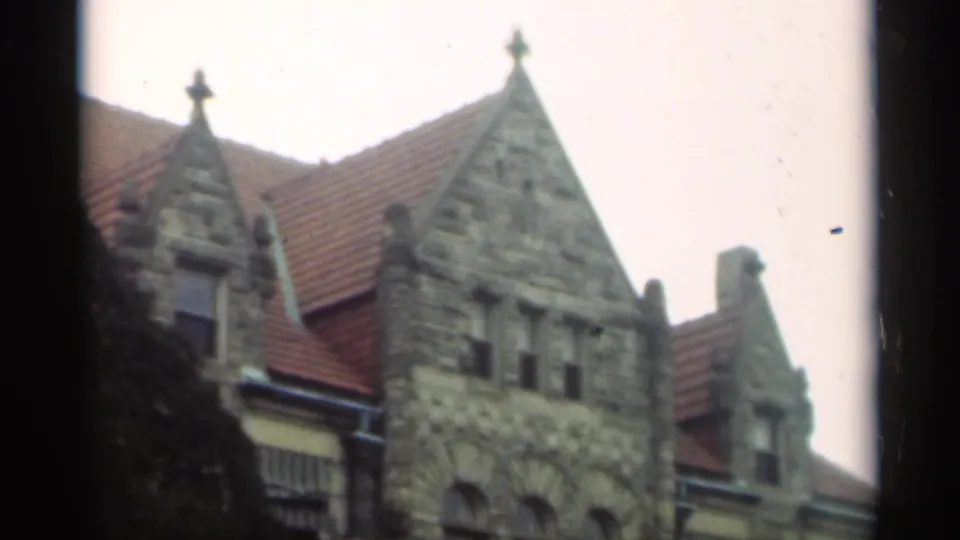 1949 New Orleans home-movie frame showing a stone gabled exterior, red tile roof, small windows, and tree branches near the facade.