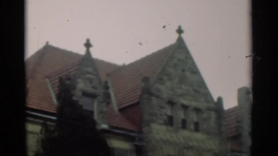 1949 New Orleans home-movie view of a stone building facade with red tile roofing, decorative gable detail, and a dark tree silhouette.