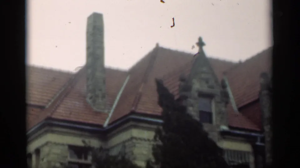 1949 New Orleans 8mm frame showing the upper portion of a historic stone house with red roof tiles, a tall chimney, and trees.