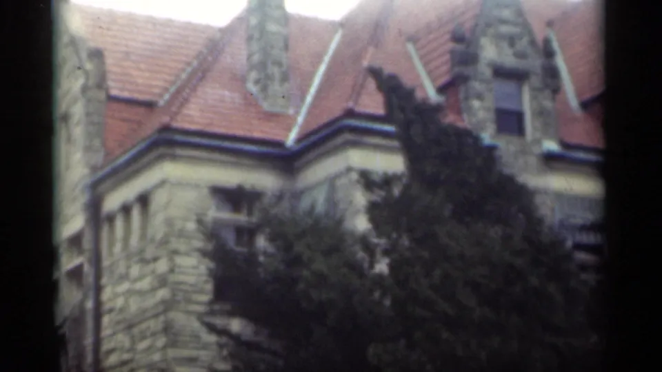1949 New Orleans 8mm frame of a stone house corner with red roof tiles, ornate gables, upper windows, and dense trees.