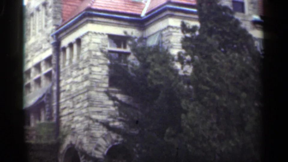 1949 New Orleans 8mm frame showing the side of a stone house with windows, roof trim, trees, and a lower arched opening.