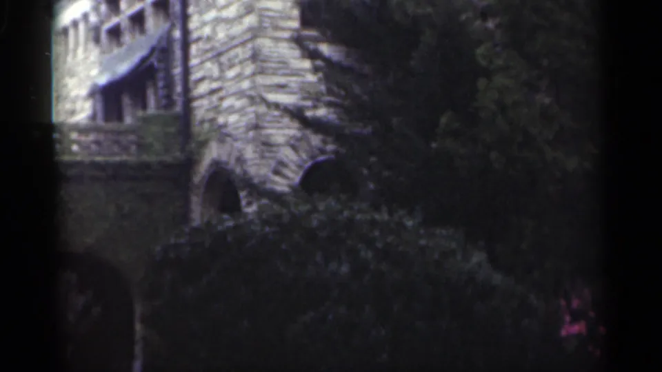 1949 New Orleans 8mm frame showing rough stone arches, ivy or foliage, and shaded garden planting around a historic-looking building.