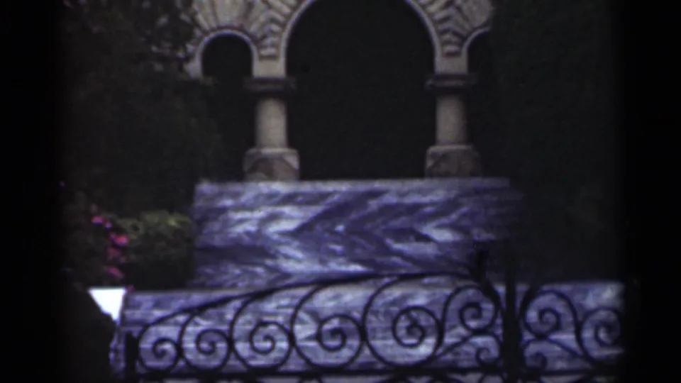 1949 New Orleans 8mm frame showing an ornate stone building facade with arched openings, columns, iron railing, greenery, and a small lamp.