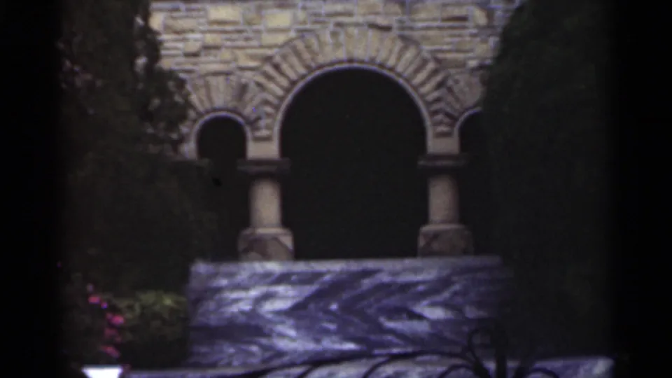 1949 New Orleans 8mm frame with arched masonry openings, columns, iron railing, and dark surrounding greenery.