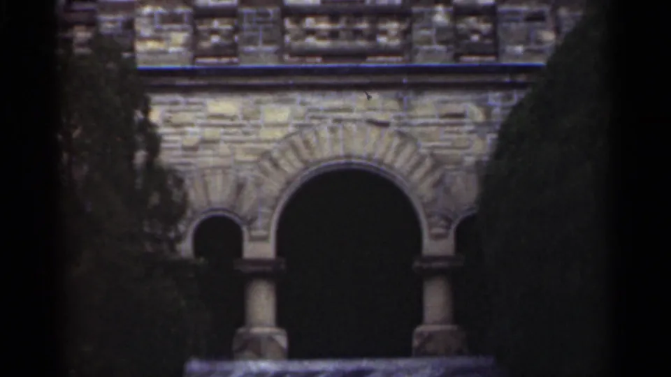 1949 New Orleans 8mm frame showing the facade during an upward tilt, with arched stonework, columns, railing, and greenery.