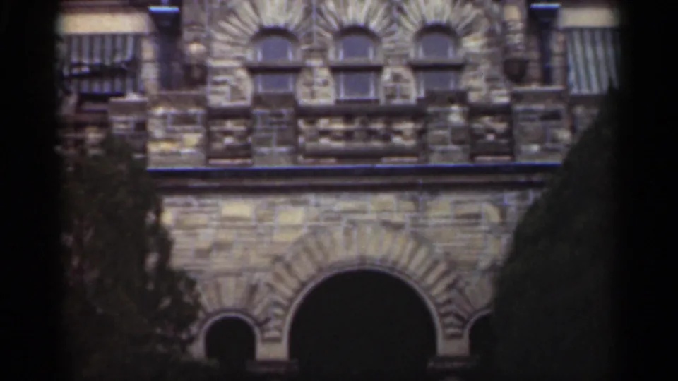 1949 New Orleans 8mm frame showing the upper facade with small arched windows, decorative stonework, railing, awnings, and trees.