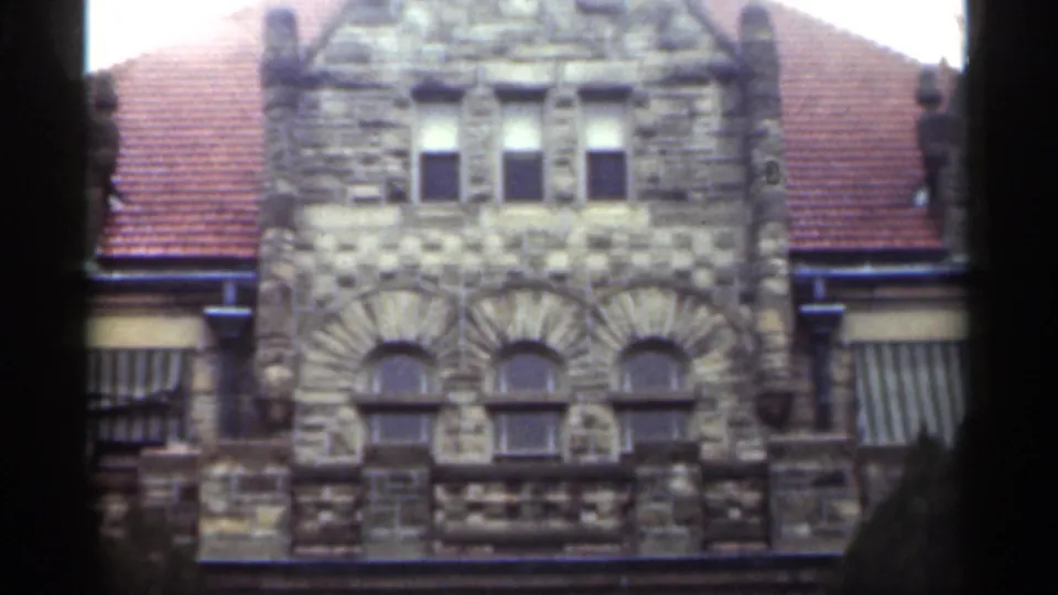 1949 New Orleans frame showing the upper facade of a stone Christian church with arched windows, roof tiles, and shaded tree edges.